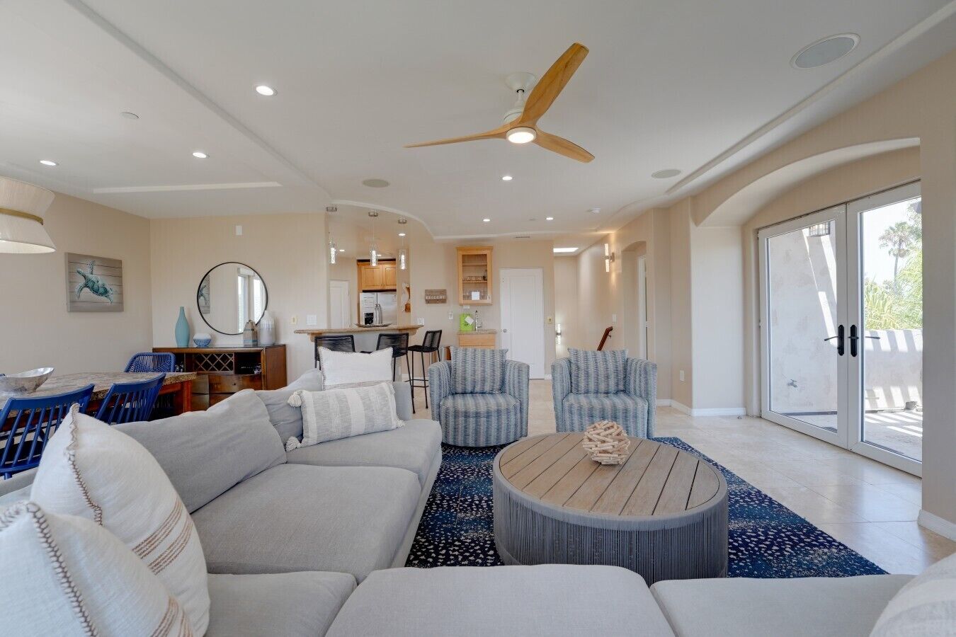 A spacious living room with a large sofa, two armchairs, a coffee table, and a ceiling fan.