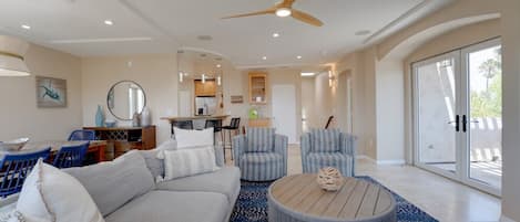 A spacious living room with a large sofa, two armchairs, a coffee table, and a ceiling fan.