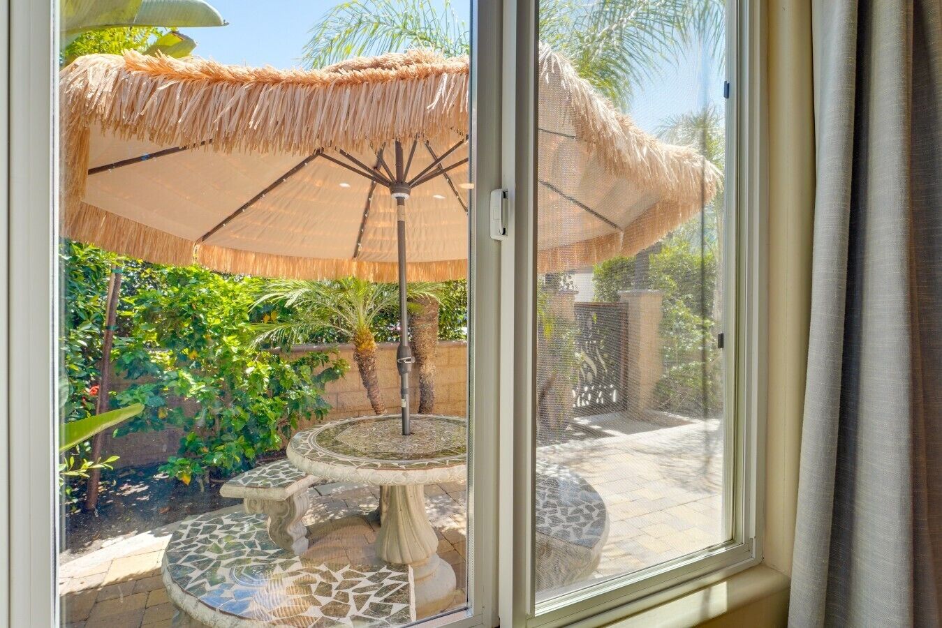 Een terras met een rieten parasol, een decoratieve fontein en weelderige beplanting.