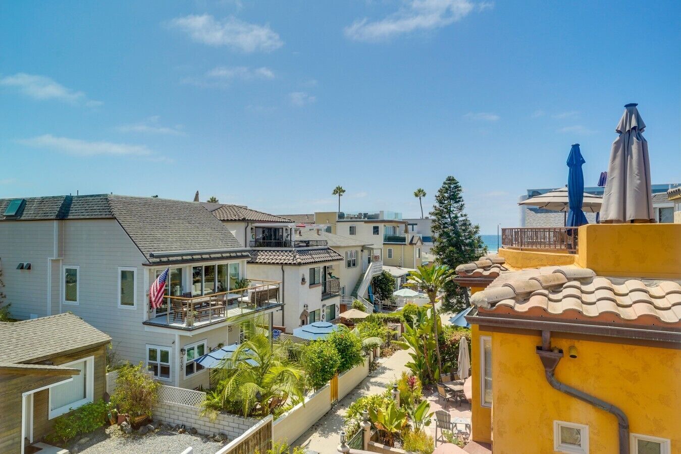 A residential area with multiple houses, a balcony with outdoor furniture, and a clear view of the ocean.