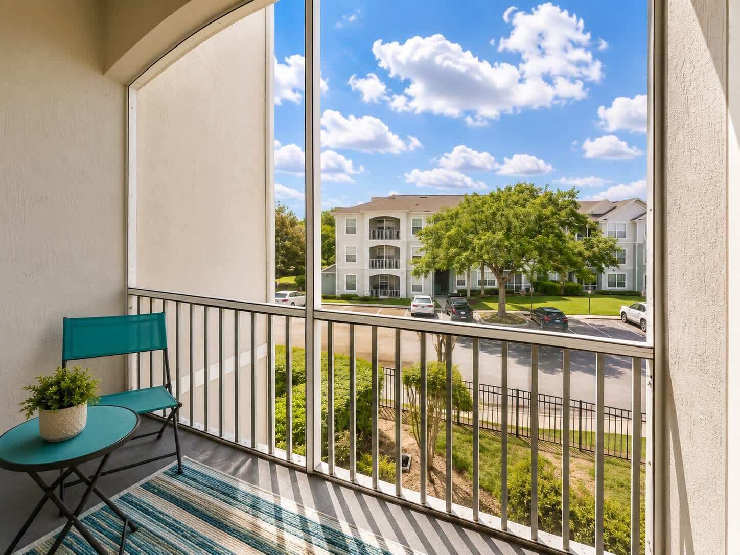 A balcony with a view of a residential area, a small table with a plant, and a chair.