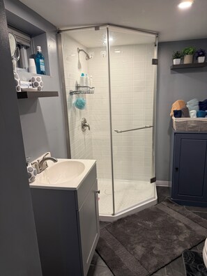 Ein modernes Badezimmer mit Duschkabine aus Glas, Waschbecken mit Waschtisch und einer kleinen Ablage für Pflegeprodukte.