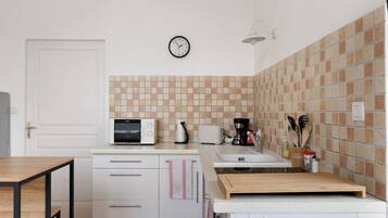 Una cocina equipada con microondas, tostadora, cafetera y un reloj en la pared.