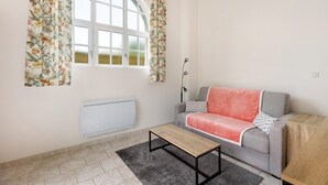 Een woonkamer met een bank, een salontafel, een radiator en een raam met bloemen gordijnen.