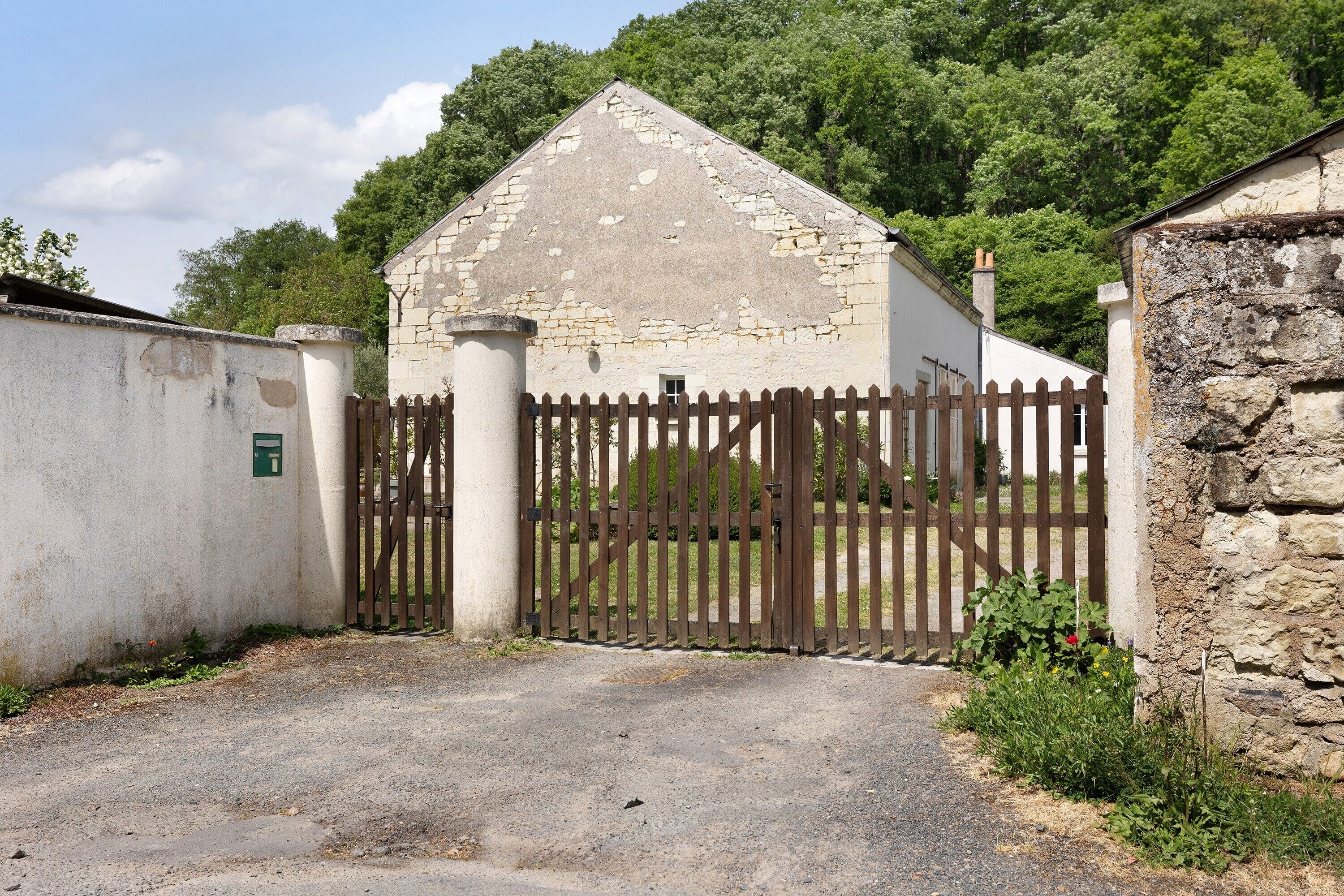 A rustic building with a stone facade, a wooden gate, and a gravel driveway.