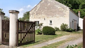 Een stenen gebouw met een houten poort, een geplaveid pad en een kleine struik.