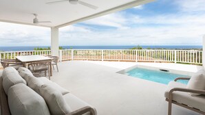 Ein überdachter Außenbereich mit Pool, weißen Möbeln und Meerblick.
