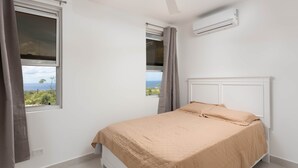 Ein Schlafzimmer mit Bett, einem Fenster mit Vorhängen, einer Klimaanlage und einem Deckenventilator.