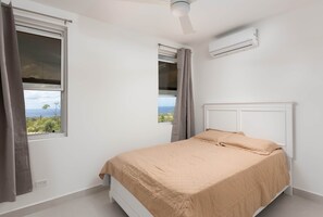 Ein Schlafzimmer mit Bett, einem Fenster mit Vorhängen, einer Klimaanlage und einem Deckenventilator.