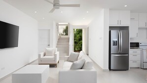 Eine moderne Küche mit integriertem Kühlschrank, einer Mikrowelle und einem Herd. Im Wohnbereich befindet sich eine weiße Couch mit Kissen und ein flachbildschirmiger Fernseher an der Wand.