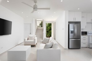 Eine moderne Küche mit integriertem Kühlschrank, einer Mikrowelle und einem Herd. Im Wohnbereich befindet sich eine weiße Couch mit Kissen und ein flachbildschirmiger Fernseher an der Wand.