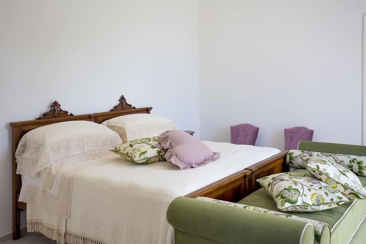 A bed with a wooden headboard, a green upholstered bench, and a white bedspread.