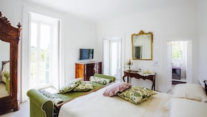 A bedroom with a bed, a green armchair, a wooden dresser, a mirror, and a television. - Palazzo Cacace Relais (Meta)