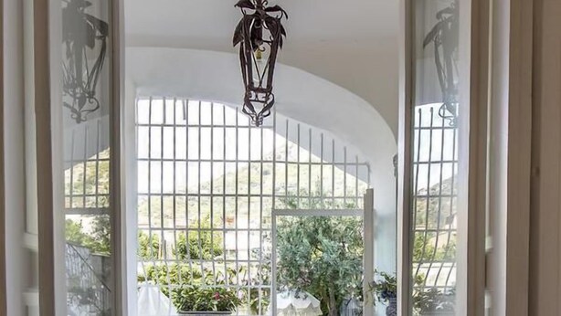 A corridor with a view of a garden through a glass door, a hanging light fixture, and a tiled floor. - Palazzo Cacace Relais (Meta)