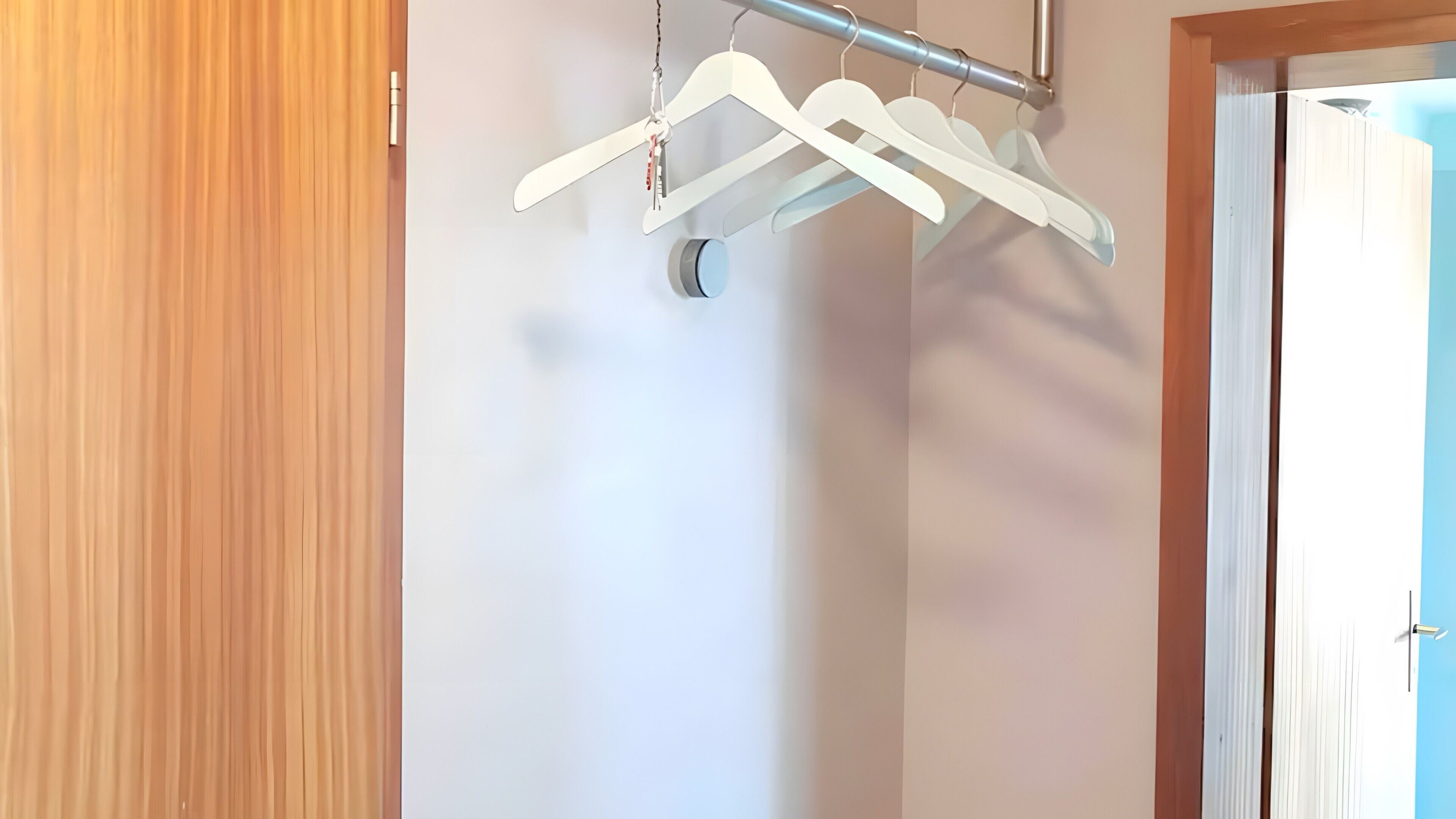 Un couloir avec une porte en bois, un mur blanc et une barre métallique sur laquelle sont accrochés des cintres blancs.
