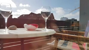 Une table avec deux verres à vin et un bol décoratif, placée sur un balcon donnant sur des immeubles.