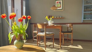 Un coin repas avec une table et des chaises en bois, un vase de tulipes et une étagère murale où sont exposés des objets en verre.
