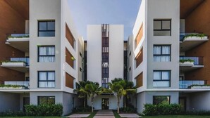 A modern multi-story building with balconies, a central vertical feature, and a symmetrical design. - Beautiful 1-Bedroom Apt en las Canas punta cana. (Punta Cana)