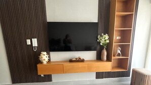 A modern living room with a flat-screen TV mounted on a wooden console, a vase with flowers, and a wooden coffee table. - Beautiful 1-Bedroom Apt en las Canas punta cana. (Punta Cana)
