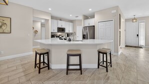 Una cocina moderna con una isla central, armarios blancos y un refrigerador de acero inoxidable.