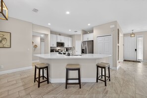 A modern kitchen with a central island, white cabinetry, and a stainless steel refrigerator. -     Family-Friendly PSL Vacation Home Near Clover Park & Beaches (Port Saint Lucie)