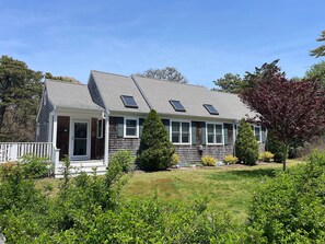 A two-story house with a porch, a small deck, and a well-maintained lawn. - Relaxing Cape Escape • Family Retreat • Walk to Beach • 6 beds • Sleeps 8 (Chatham)