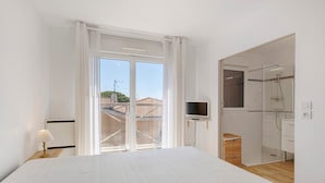 Ein Schlafzimmer mit Bett, Fernseher, Glasdusche und einem Balkon mit Blick auf Gebäude.