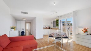 Eine moderne Wohnung mit einem roten Sofa, einem Essbereich mit Tisch und Stühlen, einer Küche und einem Balkon mit Blick auf Gebäude.