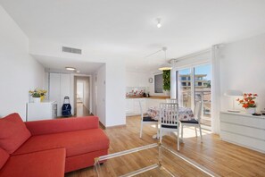 Eine moderne Wohnung mit einem roten Sofa, einem Essbereich mit Tisch und Stühlen, einer Küche und einem Balkon mit Blick auf Gebäude.