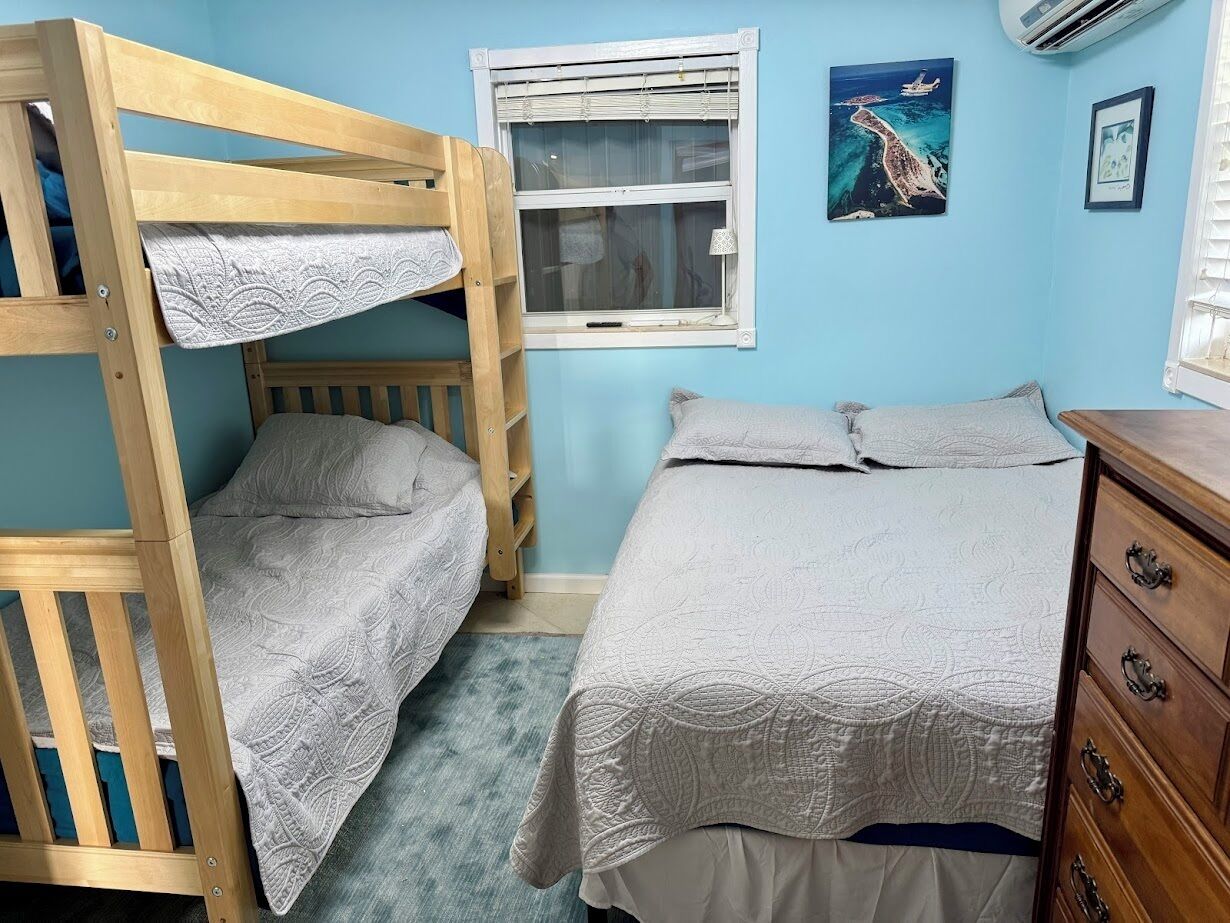 A room with bunk beds, a window with blinds, a dresser, and a framed picture on the wall.