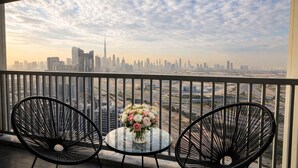Un balcon avec deux chaises et une table, donnant sur un paysage urbain composé d’immeubles modernes et d’un ciel dégagé.