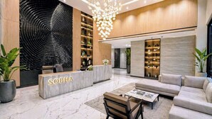 Un hall d’entrée moderne avec un comptoir de réception portant l’inscription « SOBHA », un grand lustre et un espace détente comprenant des canapés et une table basse.
