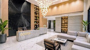 Un hall d’entrée moderne avec un comptoir de réception portant l’inscription « SOBHA », un grand lustre et un espace détente comprenant des canapés et une table basse.