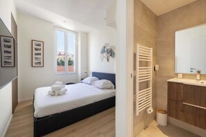 A bedroom with a bed, a bedside table, a window, and a bathroom with a sink and mirror. - Modern Apartment a/c 2ch/4p - Cannes (Cannes)