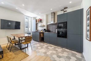A modern kitchen with dark cabinets, a wooden dining table, and a hexagonal patterned floor. - Modern Apartment a/c 2ch/4p - Cannes (Cannes)