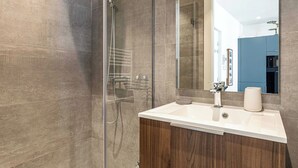 Ein modernes Badezimmer mit Duschkabine aus Glas, einem weißen Waschbecken und einem großen Spiegel.
