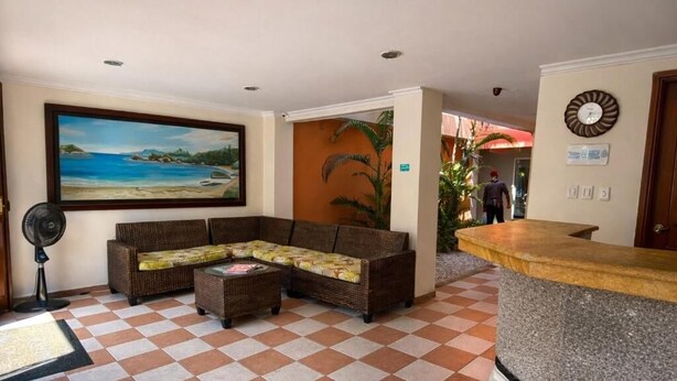 A lobby with a checkered floor, a sofa, a fan, a painting, and a reception desk. - Hotel Terranova SM (Santa Marta)