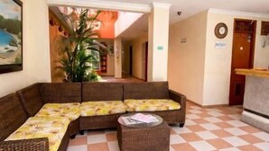 A lobby with a checkered floor, a large sectional sofa, a small round table, and a reception desk. - Hotel Terranova SM (Santa Marta)