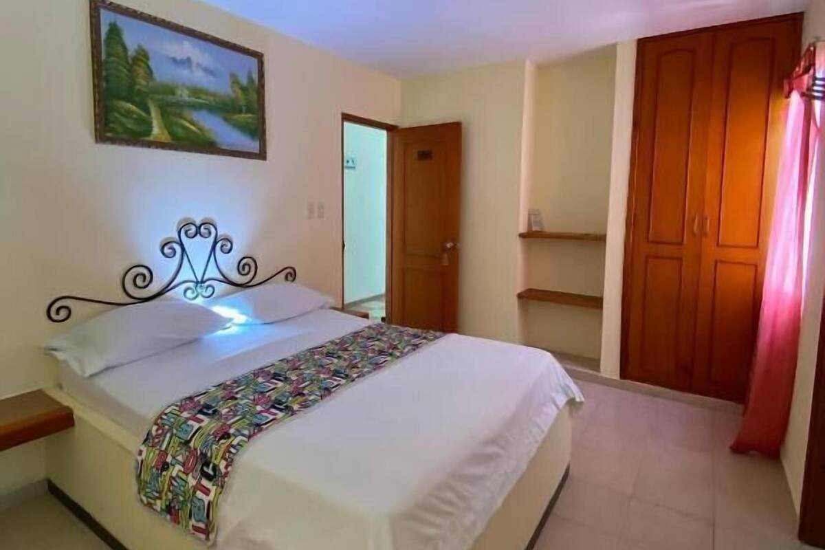 A bedroom with a bed, a painting on the wall, and a wooden wardrobe.