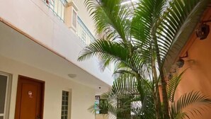 A hotel corridor with a checkered floor, a wooden door, and a large palm tree. - Hotel Terranova SM (Santa Marta)