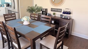 A dining area with a wooden table, chairs, a coffee station, and a kitchen in the background. - 3BR Near Downtown Kannapolis & Ballpark (Kannapolis)