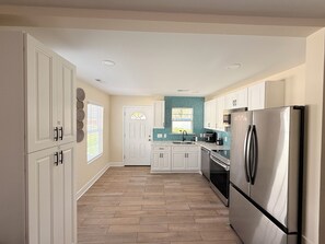 Una cocina con armarios blancos, un refrigerador de acero inoxidable y una ventana con persianas.
