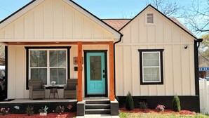 Een twee verdiepingen tellend huis met een veranda, een turquoise deur en een kleine voortuin met rode bloemen.