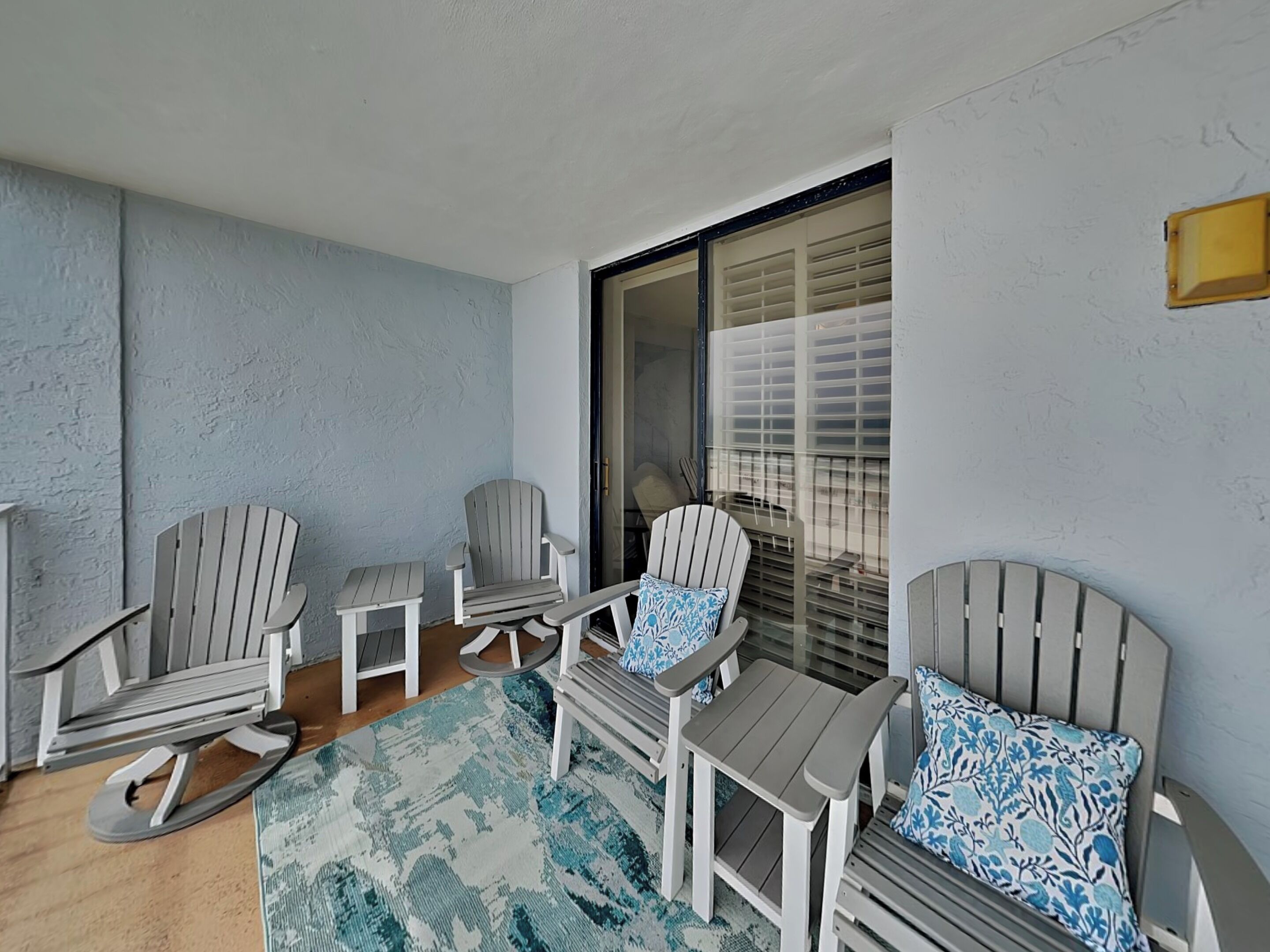 A balcony with Adirondack chairs, a small table, and a patterned rug.
