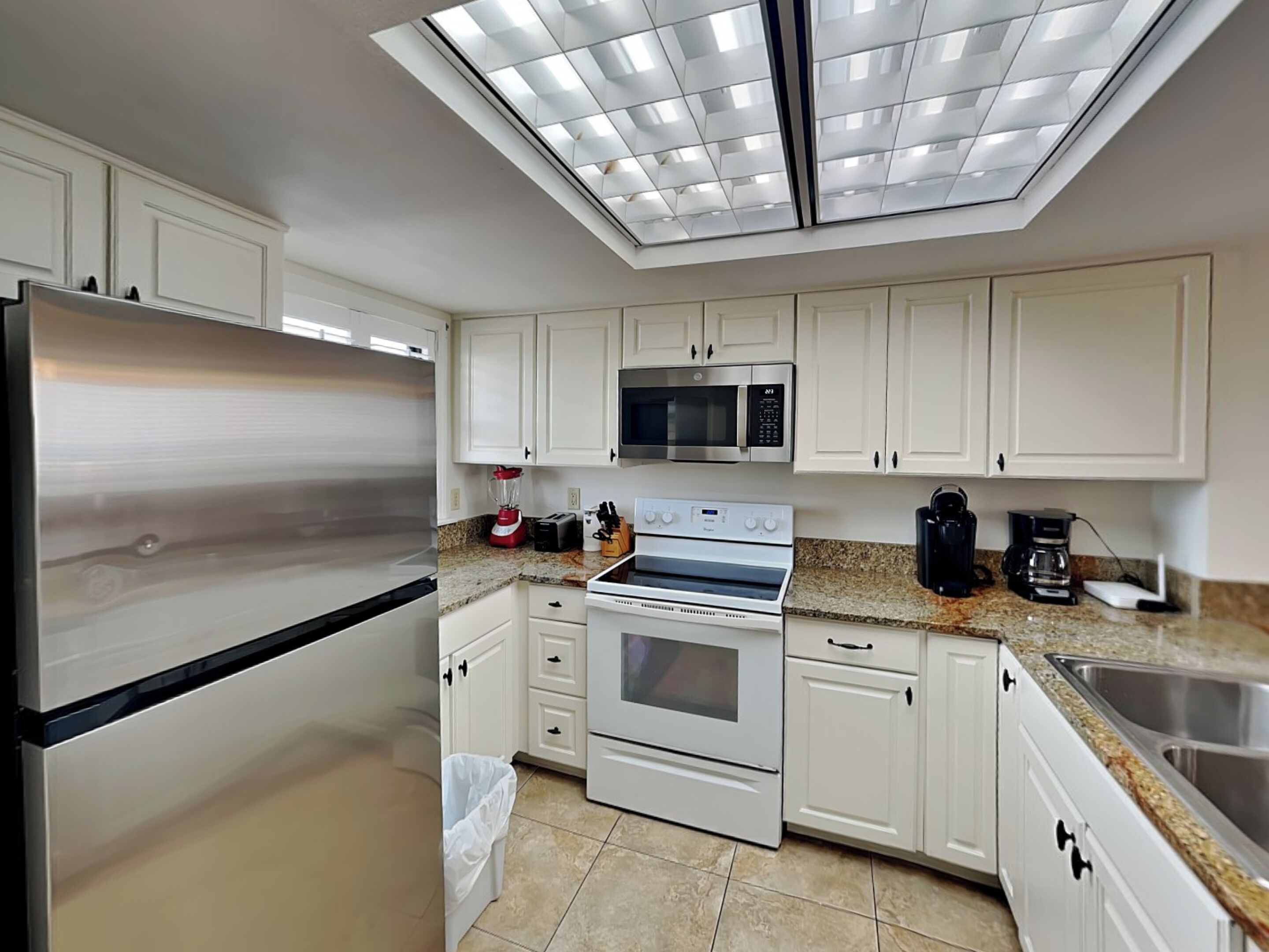 A modern kitchen with white cabinets, stainless steel appliances, and a skylight.