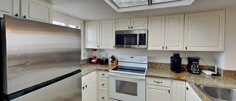 A modern kitchen with white cabinets, stainless steel appliances, and a skylight.