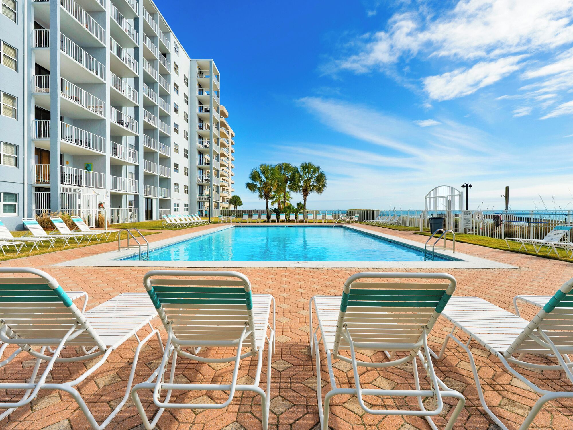 A swimming pool with lounge chairs, a building with balconies, and a clear sky.