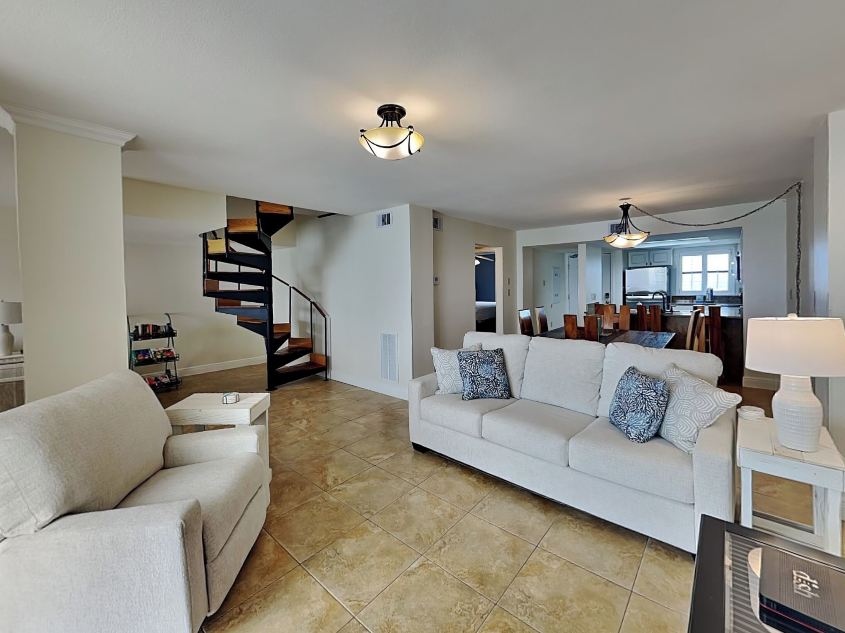 A spacious living area with a sofa, a coffee table, a dining table with chairs, a staircase, and a kitchen area.