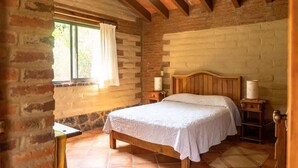 A bedroom with a wooden bed, a window with a curtain, a nightstand, and a lamp.