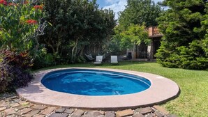A swimming pool with a stone border, surrounded by a grassy lawn and trees.